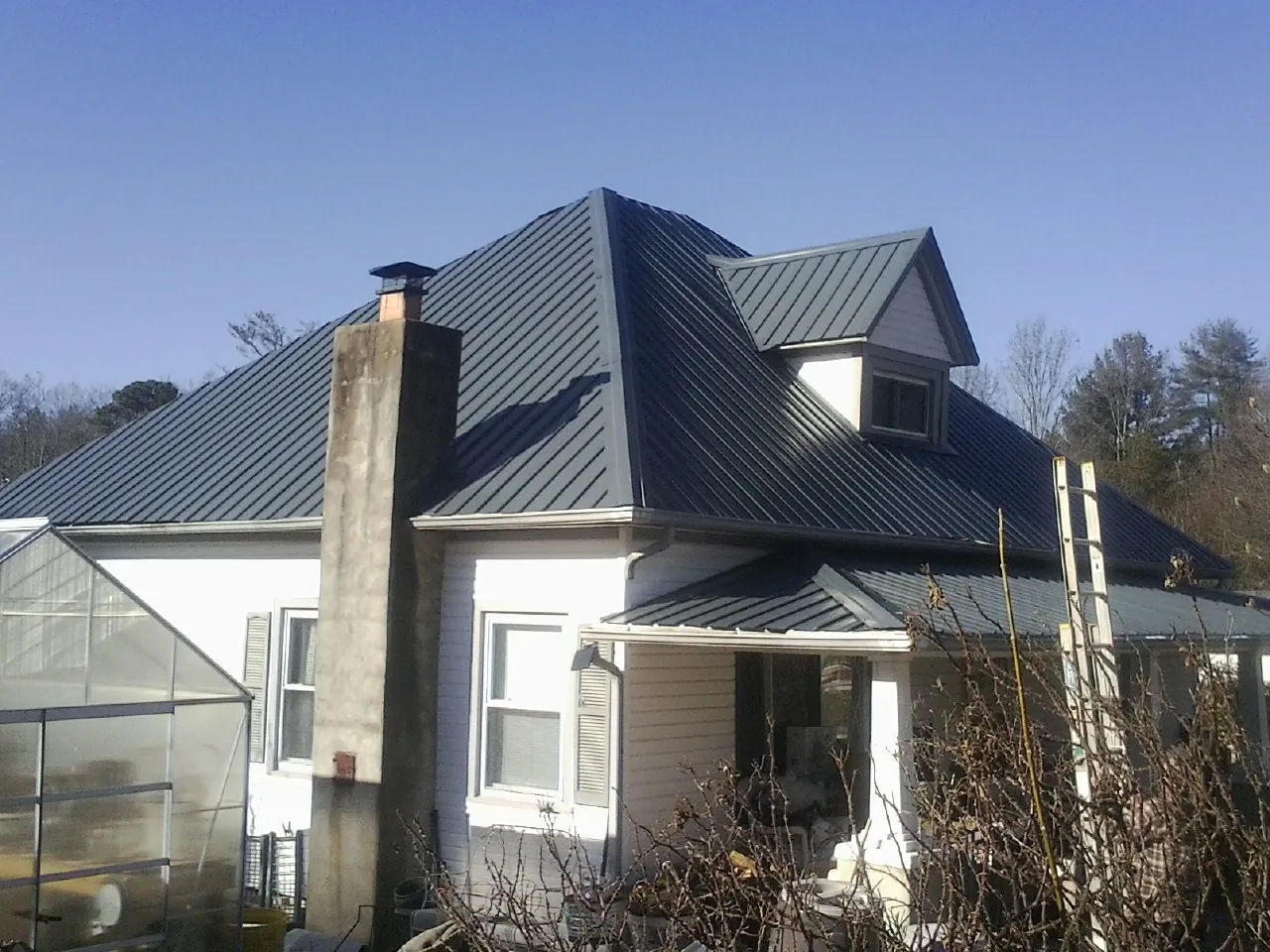 Dark blue standing seam metal roof on a white farmhouse with dormer — Slate & Tile Roof Repair by Roofing Brothers in Whitestown