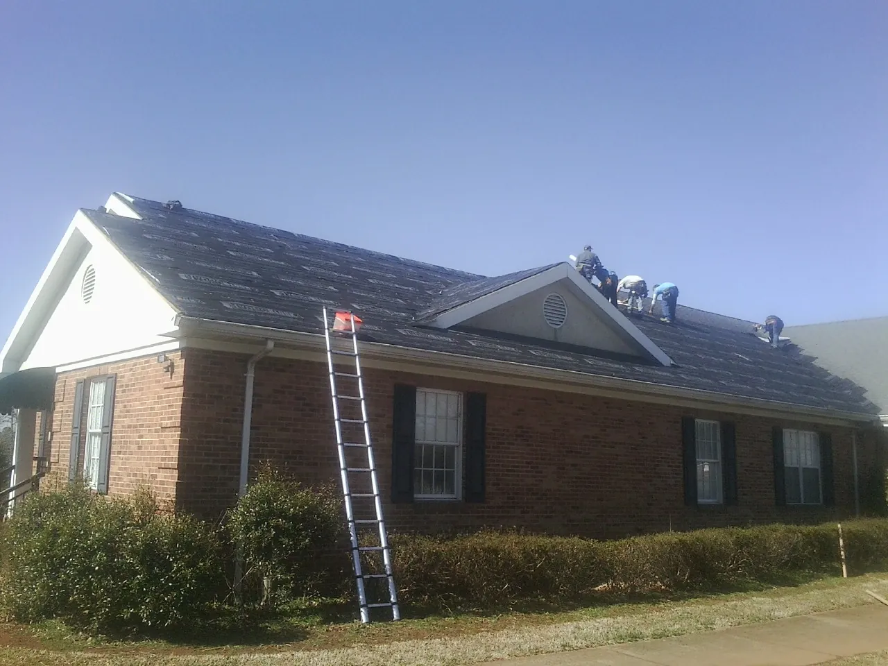 Crew tearing shingles off a brick ranch roof with a ladder set — Emergency Roof Repair work by our crew in Whitestown