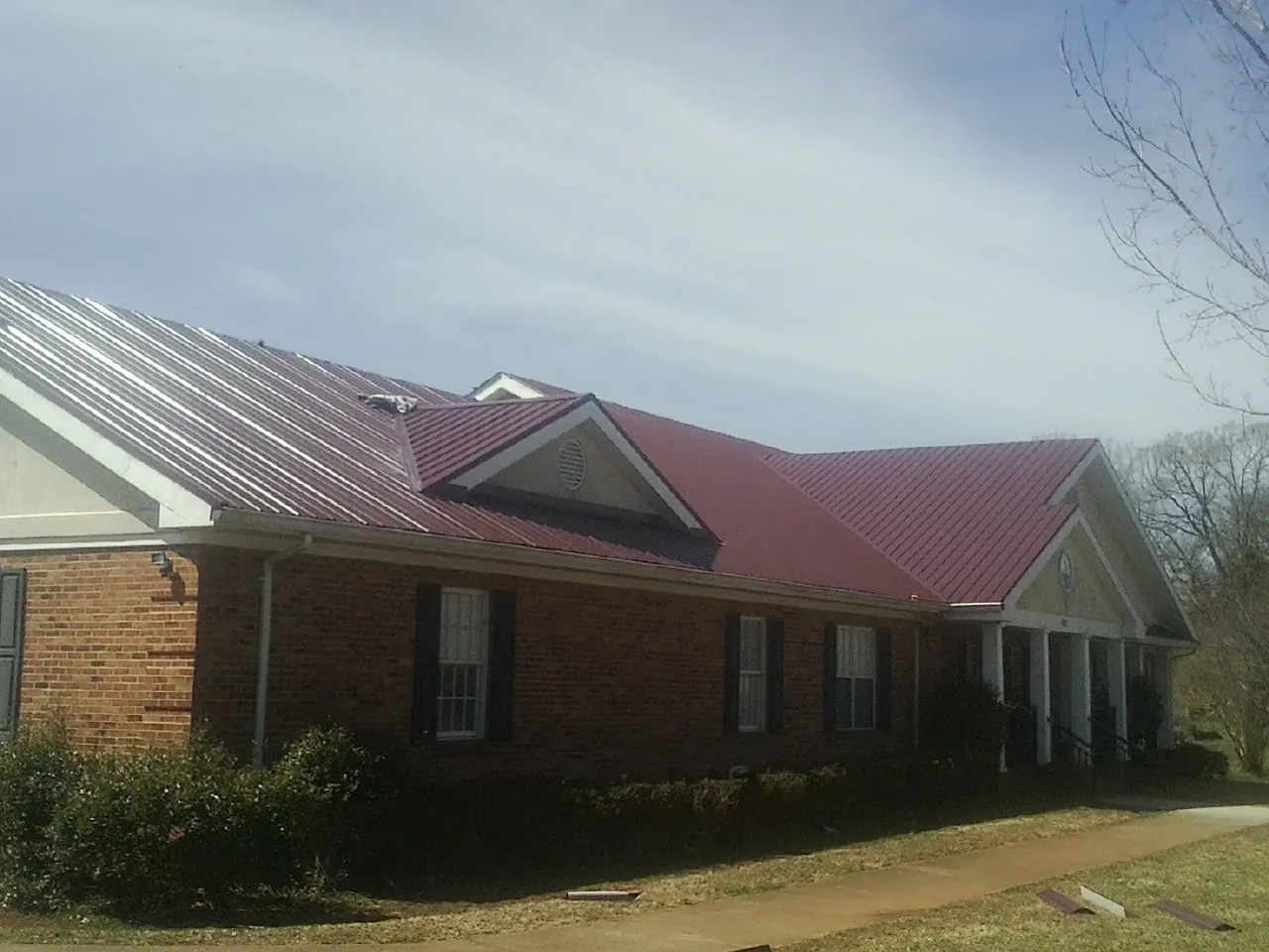 Red metal roof with gabled entries on a long brick building, from a Hail Damage Roof Repair job in Whitestown