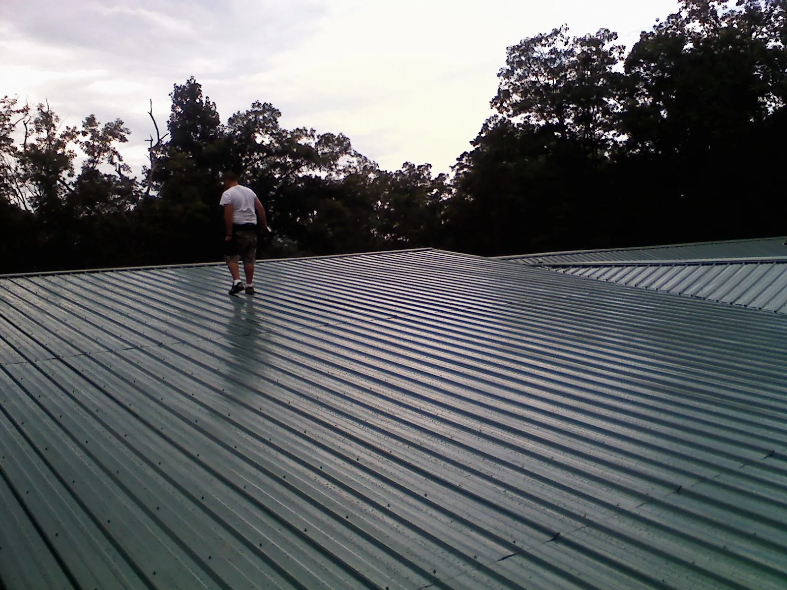 Roofer walking a wide expanse of new green metal roofing in Whitestown