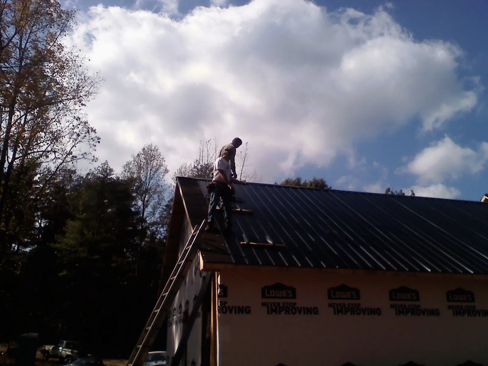 Roofer fastening dark metal panels high against a cloudy sky, from a Roof Inspection job in Whitestown