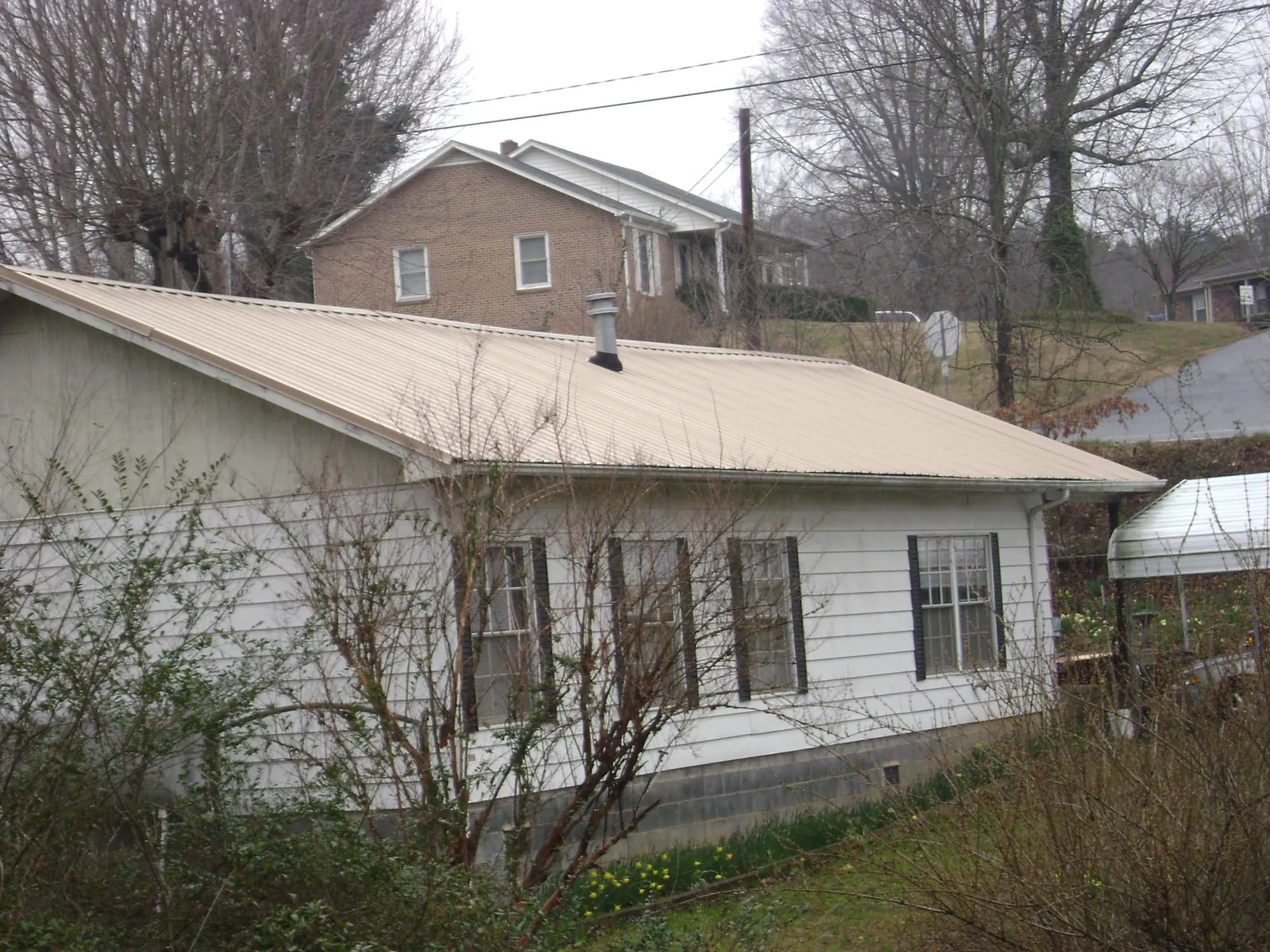 Tan metal roof on a white sided house set into a hillside — Commercial Roofing by Roofing Brothers in Whitestown